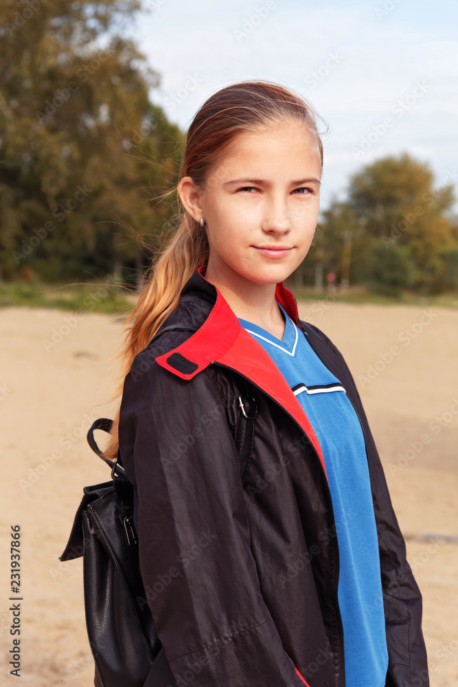 Teenager girl in a raincoat and backpack walk outdoors