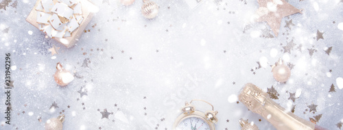 Christmas or New Year composition, frame, gray background with gold Christmas decorations, stars, snowflakes, balls, alarm clock, gift box, glasses and bottle of champagne, banner, top view