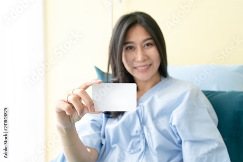 Smiling female patient on bed showing blank credit card.