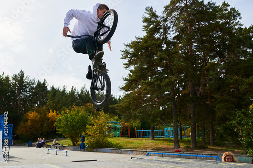 Full length portrait of modern young man doing stunts on bmx bike jumping high over ramps in skateboarding park, copy space