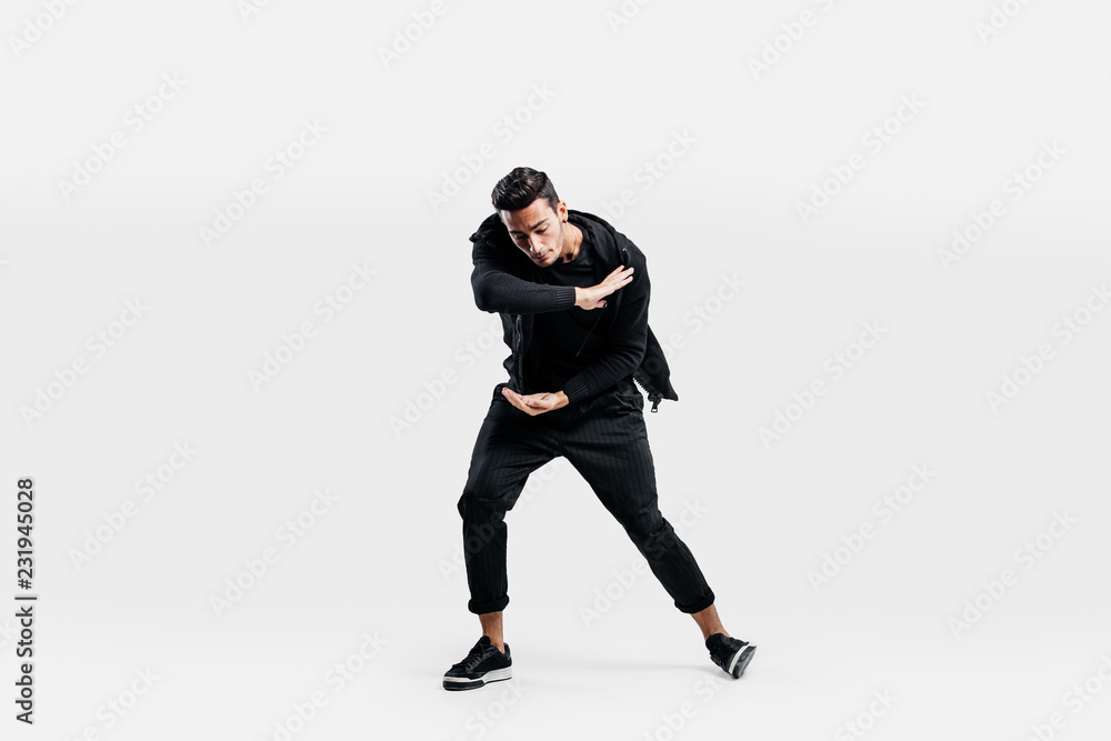 Dark-haired stylish man dressed in a stylish black clothes is dancing street dance. He makes stylized movements with his hands Dark-haired stylish man dressed in a stylish black clothes is dancing street dance. He makes stylized movements with his hands
