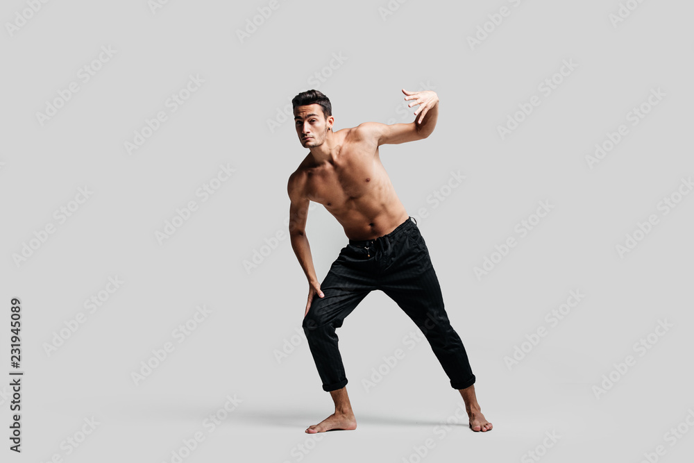 Dark-haired handsome young dancer with bare torso wearing a black pants makes dancing movements on a white background Dark-haired handsome young dancer with bare torso wearing a black pants makes dancing movements on a white background