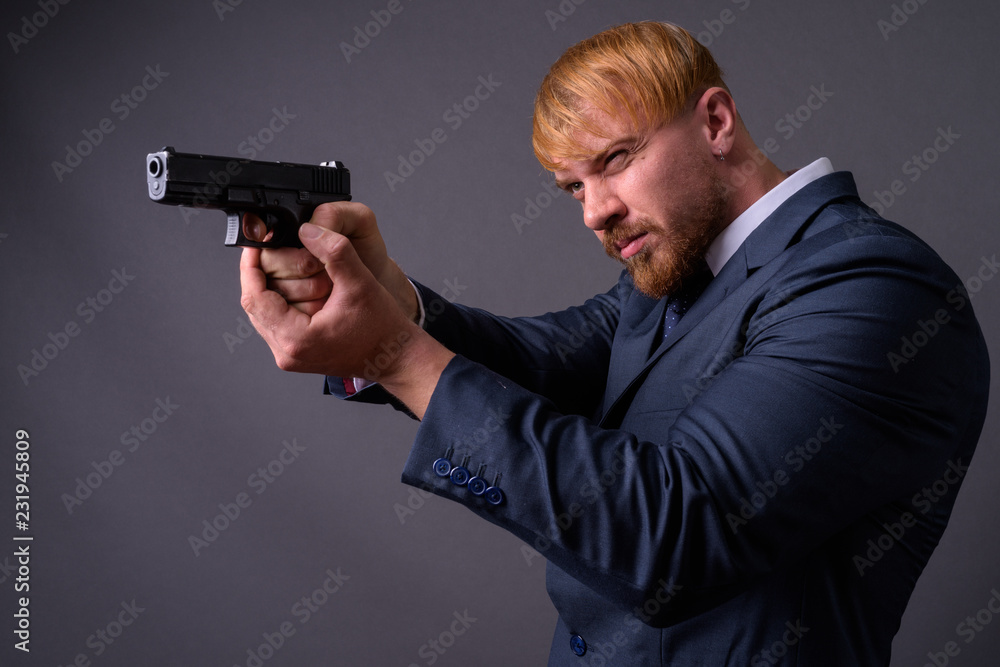 Bearded businessman with handgun against gray background Bearded businessman with handgun against gray background