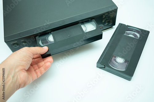 VHS videocassette is put into the video recorder to watch the video, another video cassette is on the video-tape recorder