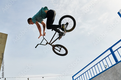 Side view portrait of young man doing bmx stunts jumping up high against sky over ramp in extreme sports park, copy space