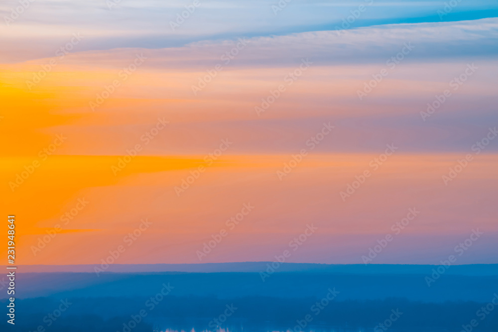 Varicolored striped surreal sky with shades of blue, cyan, pink, purple, magenta colors with cobalt land and lake. Horizontal lines of smooth clouds. Atmospheric image of tender sky, land and river.