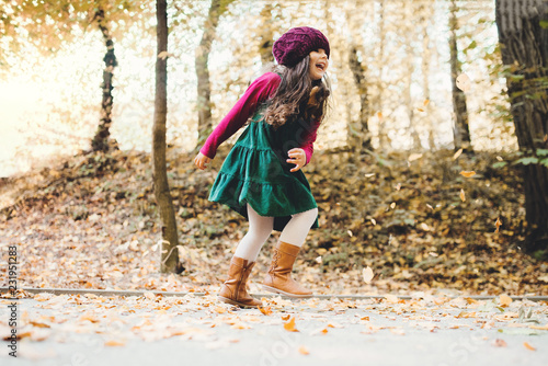 A portrait of a small toddler girl running in forest in autumn nature.