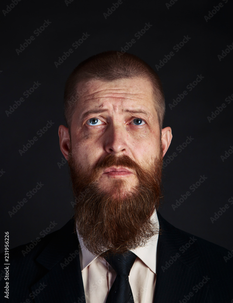 puzzled sad bearded middle-aged businessman looks up with hope and request. Close-up portrait on black background puzzled sad bearded middle-aged businessman looks up with hope and request. Close-up portrait on black background