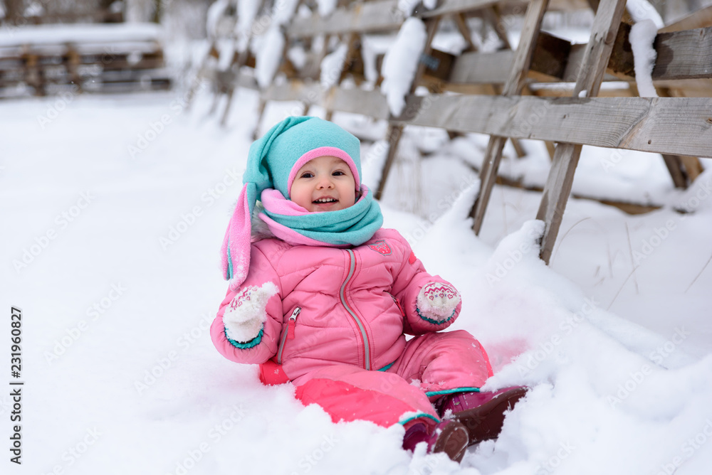 little girl in a pink jumpsuit walks in a snowy winter park little girl in a pink jumpsuit walks in a snowy winter park