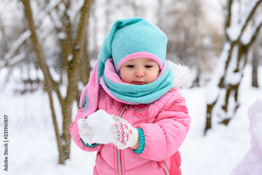little girl in a pink jumpsuit walks in a snowy winter park