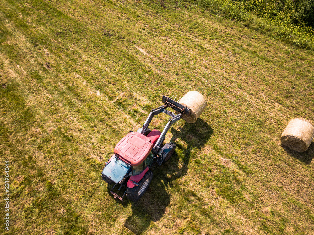 Aerial Drone Photo of Farmer Harvesting Hay Rolls in the Wheat Field with a Red Tractor Aerial Drone Photo of Farmer Harvesting Hay Rolls in the Wheat Field with a Red Tractor