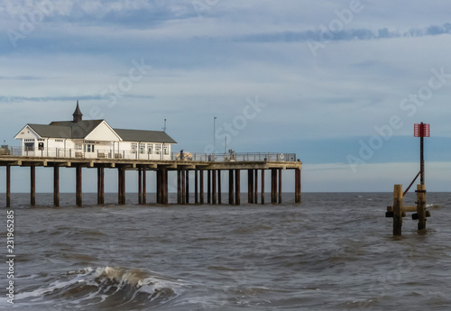Landscape view of a vintage Pier, from the public beach, with metal groyne marker. Wave breaking on foreshore. Blue sky with horizontal cloud formation. England