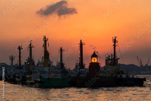 マストの柱が並ぶ岸壁の灯台に沈む夕日