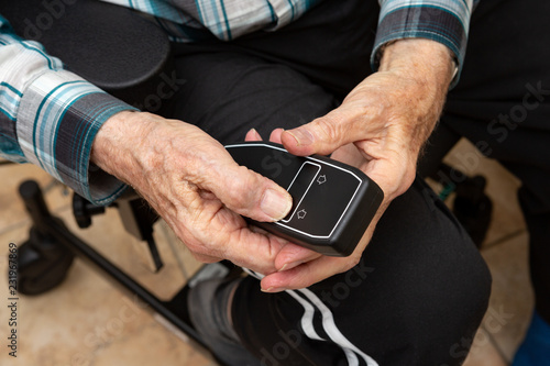 An elderly man pusching a black remote control of a electric weelchair