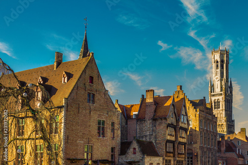 Medieval buildings with brick walls  gabled roof and Belfry bell tower in background against a blue sky  sunny day for tourism in Bruges  province of West Flanders  Belgium