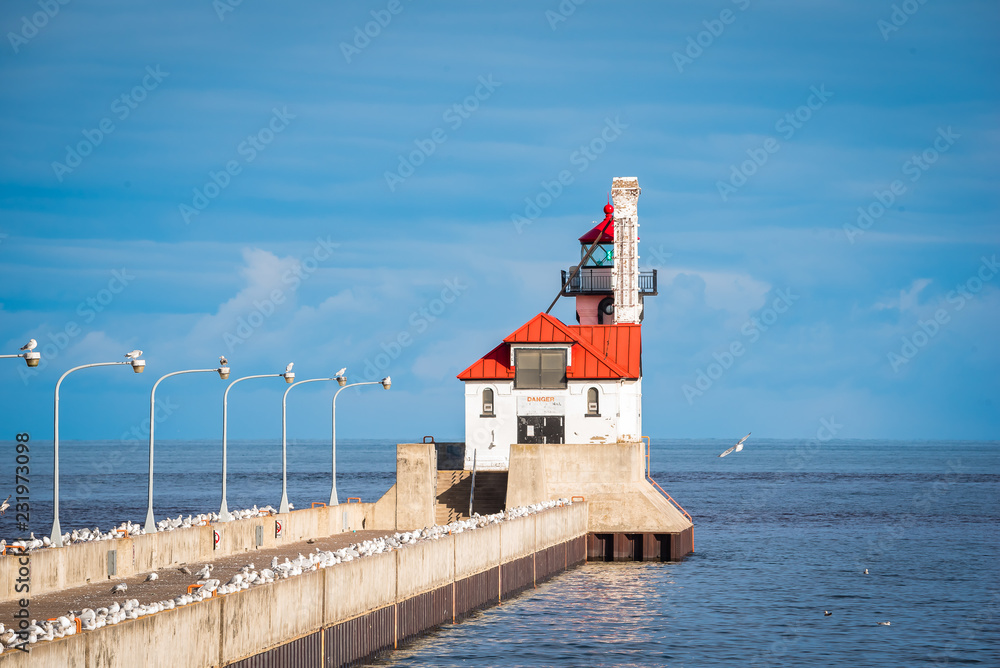 white light house, red roof out on pier, on a bright sunny blue sky day with wispy clouds.