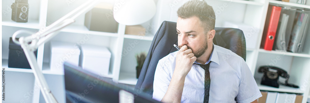 A man sits in a chair in the office and holds a pencil in his hand. On the back of the chair hangs his jacket. A man sits in a chair in the office and holds a pencil in his hand. On the back of the chair hangs his jacket.