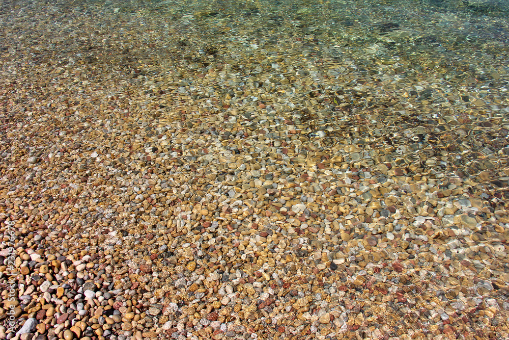 Pebbles texture diagonal covered by blue sea water