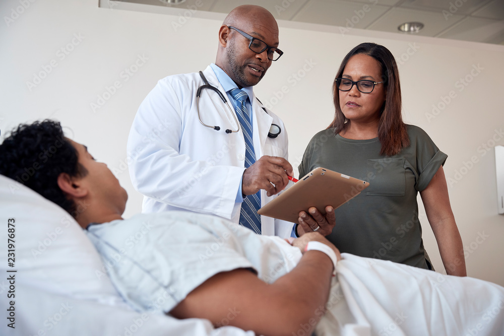 Man lying in bed and woman talking to doctor Man lying in bed and woman talking to doctor