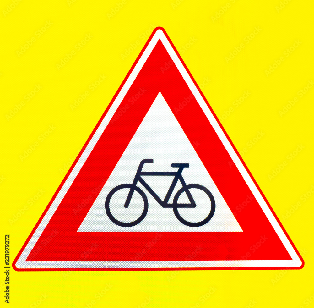 A red triangle beware of cyclists warning sign on a yellow background A red triangle beware of cyclists warning sign on a yellow background