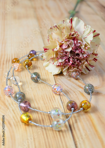 Murano glass beads and white carnation on a wooden table. Composition with flowers and handmade jewelry.