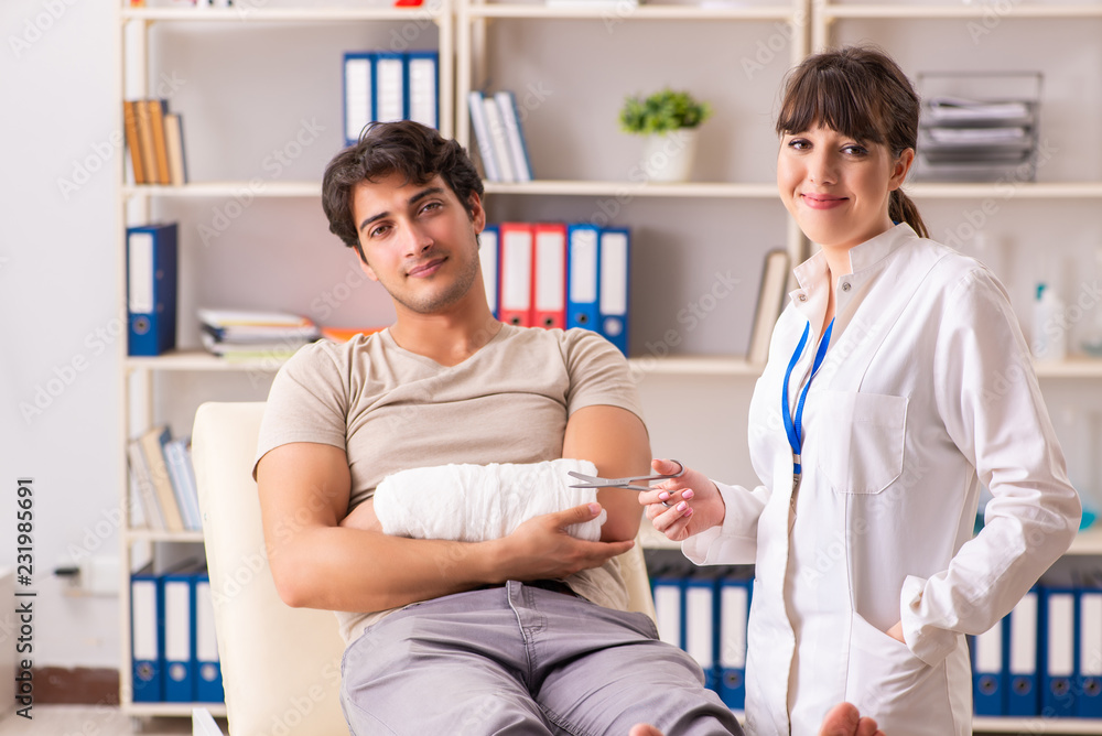 Fototapeta premium Young man with bandaged arm visiting female doctor traumatologis