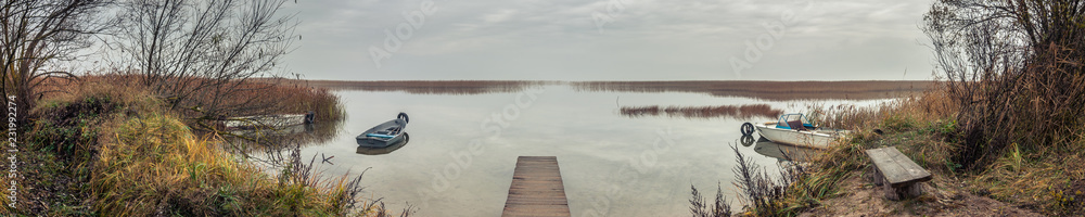 panoramic view from the coast to the lake bay with a wooden pier and boats in the autumn twilight in cloudy weather