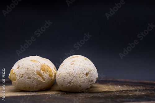 Traditional brazilian cheese bread from Minas Gerais called "Pao de Queijo" on a wooden cutting board isolated in dark background.