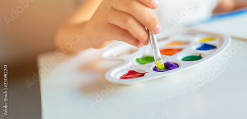 Close up of kid’s hand holding paint brush with watercolors in palette