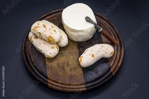 Cheese bread and brazilian minas white cheese on a wooden cutting board isolated in dark background