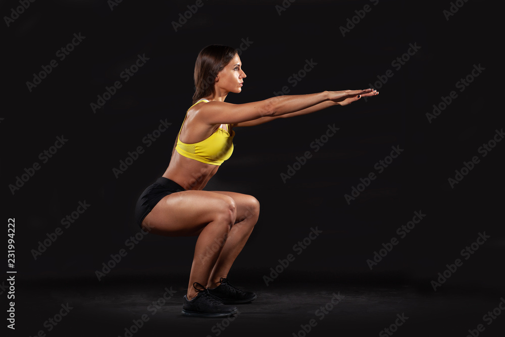 brunette muscular woman doing squats isolated on black background brunette muscular woman doing squats isolated on black background