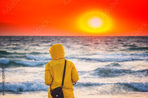 Beautiful sunrise above the stormy sea with girl in the hood looking into the distance, seascape