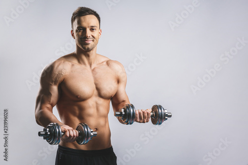 Muscular bodybuilder guy doing exercises with dumbbell over white background.