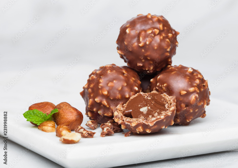 Luxury chocolate candies with hazelnuts pieces and mint leaf on marble board.