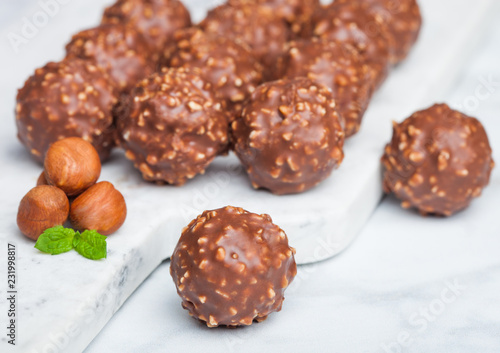 Fotografie Luxury chocolate candies with hazelnuts pieces and mint leaf on marble board
