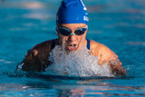 Pool water illuminated by afternoon sun cascades of the face of female swimmer as she comes up for air during breast stroke.