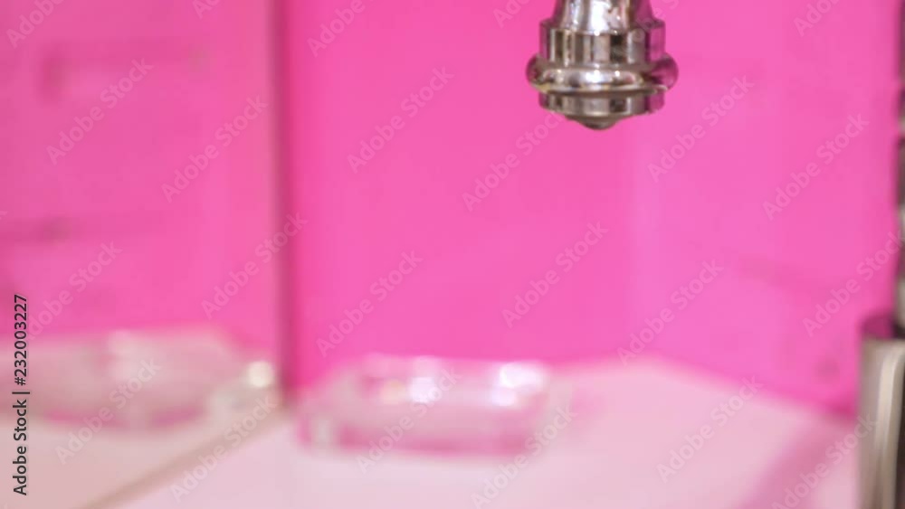 Modern faucet with dropping water at apartment with pink walls Modern faucet with dropping water at apartment with pink walls
