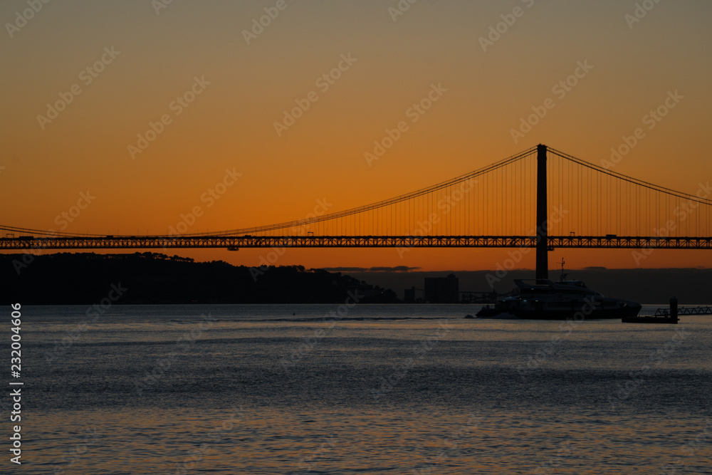 Fototapeta premium Sunset view of Tagus river (Rio Tajo) and 25th of April Bridge (Ponte 25 de Abril). Lisbon, Portugal