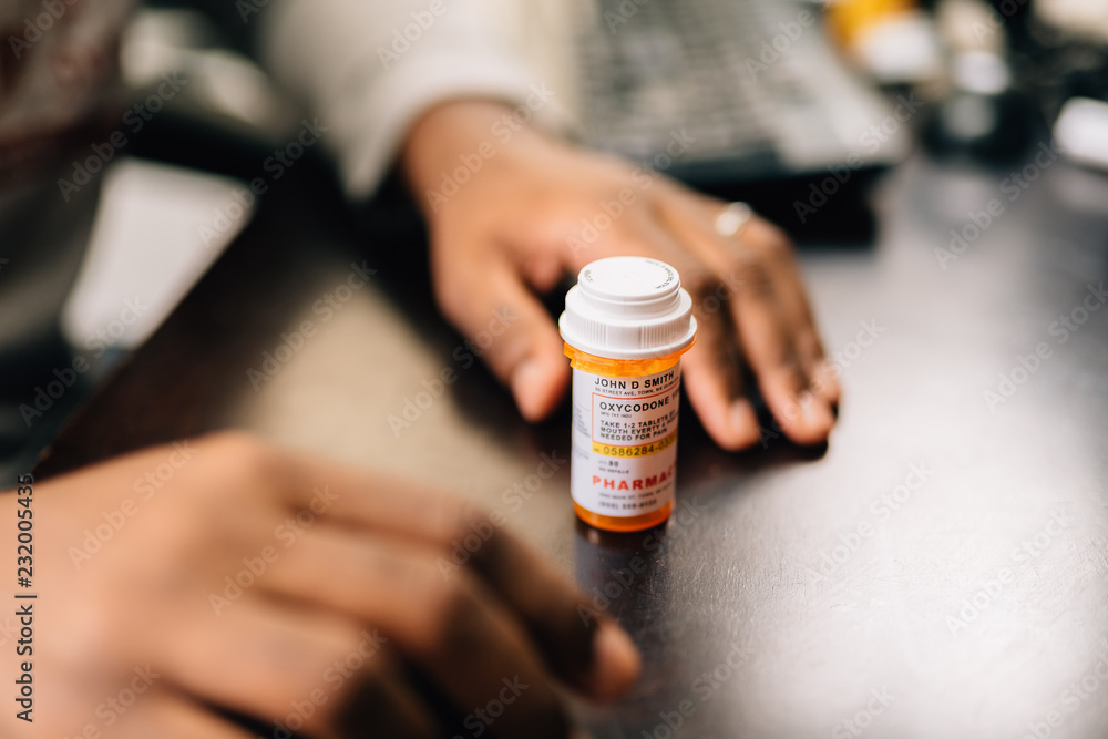 african american man taking opioid pills sitting at a dark table - obrazy, fototapety, plakaty 