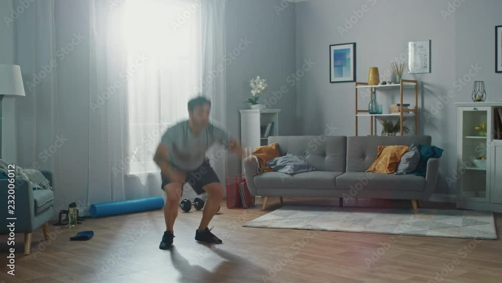 Muscular Athletic Fit Man in T-shirt and Shorts is Doing Jack Burpee Exercises at Home in His Spacious and Bright Apartment with Minimalistic Interior. Muscular Athletic Fit Man in T-shirt and Shorts is Doing Jack Burpee Exercises at Home in His Spacious and Bright Apartment with Minimalistic Interior.