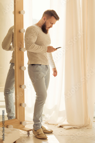 Bodybuilder with a cell phone. Muscular man with a beard in a tight t-shirt holding a phone. Stylish and sporty young man.