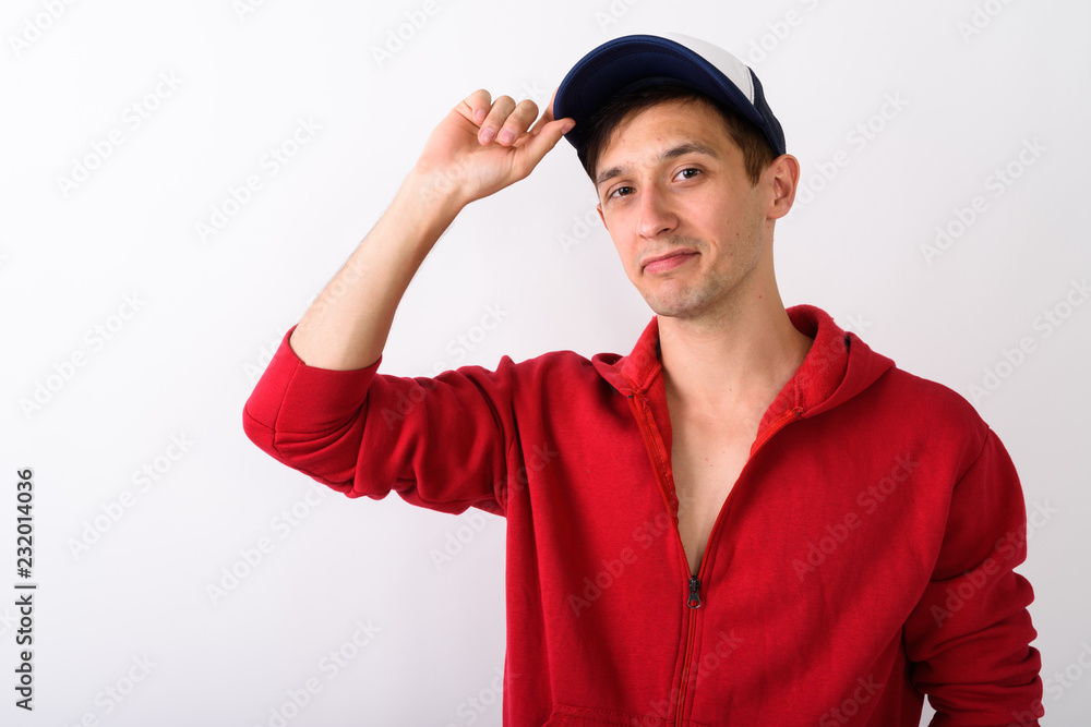 Studio shot of young handsome man wearing and holding cap agains Studio shot of young handsome man wearing and holding cap agains