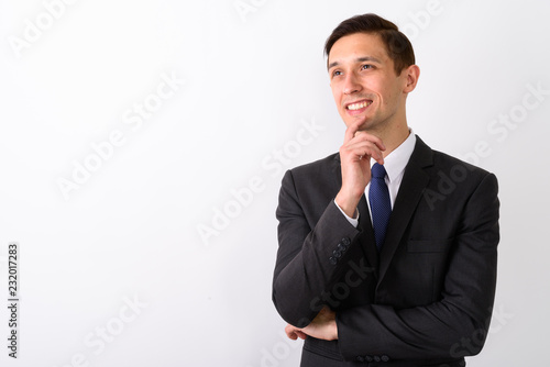 Studio shot of young happy businessman smiling and thinking whil
