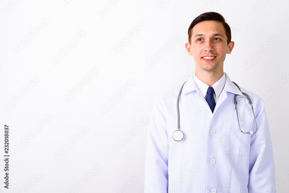 Studio shot of young happy man doctor smiling and thinking while Studio shot of young happy man doctor smiling and thinking while