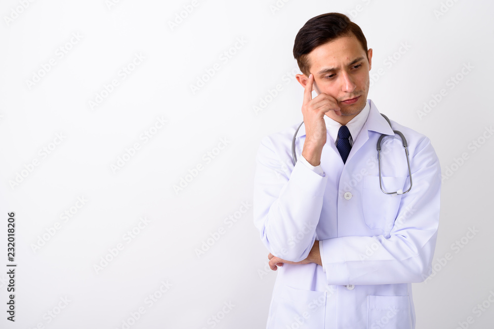 Studio shot of young handsome man doctor thinking with finger on Studio shot of young handsome man doctor thinking with finger on