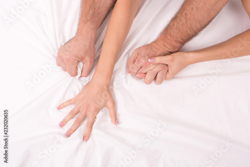 Hands of couple who making love in bed on white crumpled sheet, focus on hands