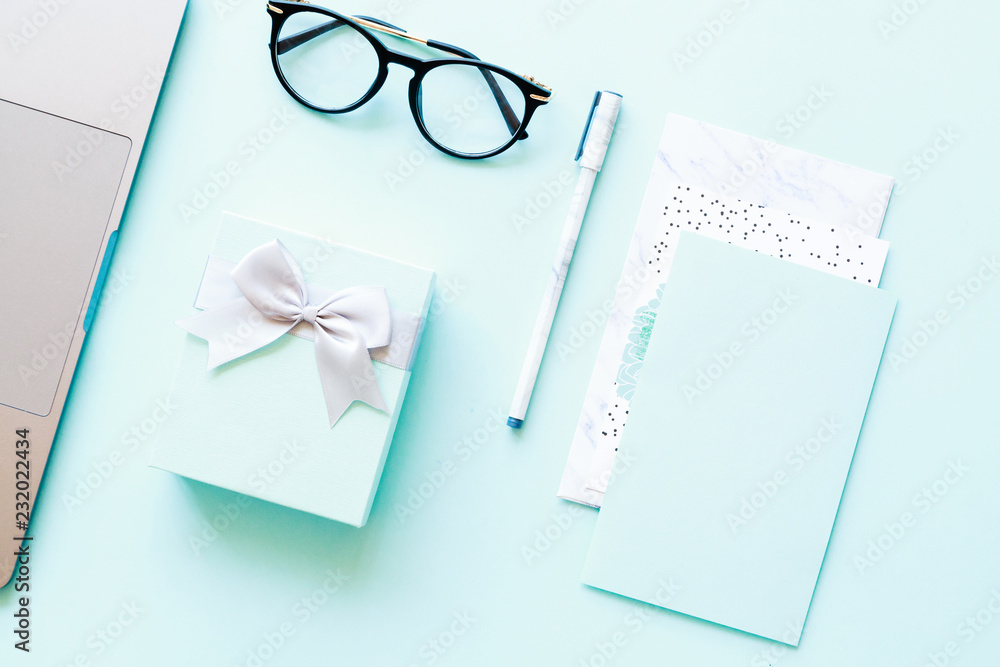 Flatlay of laptop, paper, pen, reading glasses and little gift box on a blue background Flatlay of laptop, paper, pen, reading glasses and little gift box on a blue background