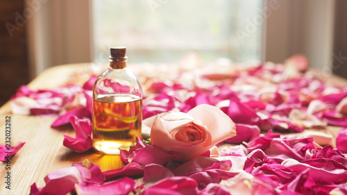 Bottle of aroma oil with roses petals on wooden surface, selected focus