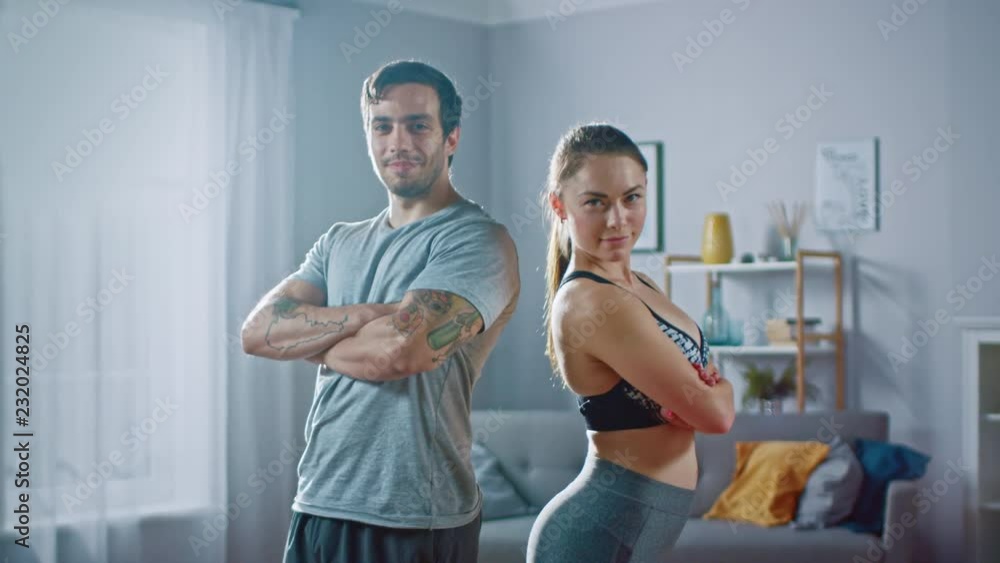 Muscular Athletic Man and Beautiful Fitness Woman in Workout Clothes are Confidentally Posing in Their Bright and Spacious Apartment with Minimalistic Interior. Muscular Athletic Man and Beautiful Fitness Woman in Workout Clothes are Confidentally Posing in Their Bright and Spacious Apartment with Minimalistic Interior.