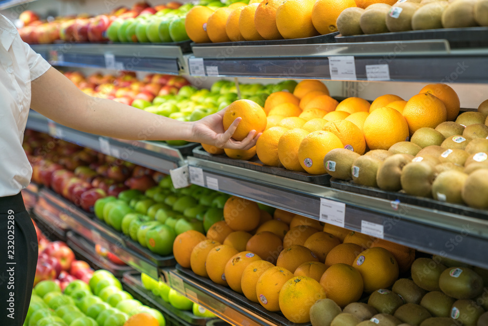 Fresh healthy fruits on shelves in supermarket. With a woman hand choosing best fruits Fresh healthy fruits on shelves in supermarket. With a woman hand choosing best fruits